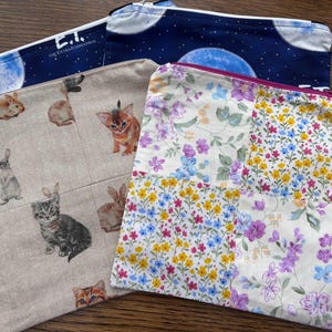 May include: Four rectangular zipped pouches. One features a dark blue space print with the text E.T. The Extra-Terrestrial. One is a beige fabric with various rabbit and kitten illustrations. Two pouches feature patchwork floral patterns in pastel colours.