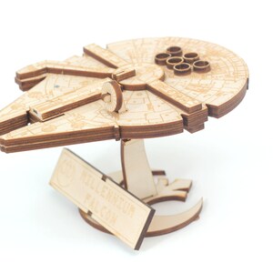 May include: A wooden model of the Millennium Falcon spaceship from Star Wars. The model is assembled and has a plaque that reads "Millennium Falcon".