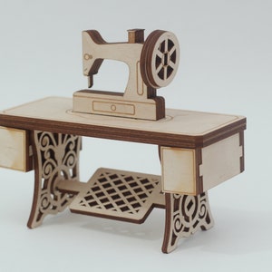 Könnte beinhalten: Ein Holzmodell einer Vintage-Nähmaschine mit einem dekorativen Sockel und einem Fußpedal. Die Maschine ist aus hellbraunem Holz gefertigt und hat einen weißen Hintergrund.