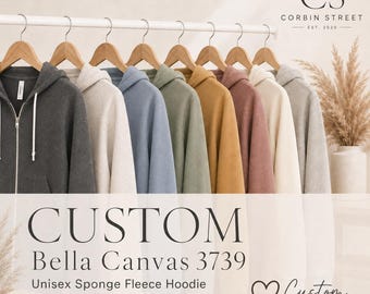 May include: A collection of Bella Canvas 3739 full-zip hoodies hanging on wooden hangers in various colors including charcoal, cream, blue, sage green, mustard yellow, mauve, and light gray. Text reads: CUSTOM Bella Canvas 3739 Unisex Sponge Fleece Hoodie.