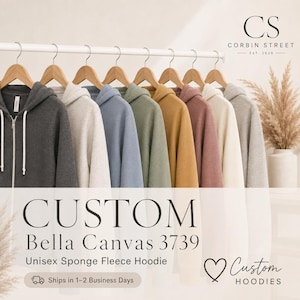 May include: A row of Bella Canvas 3739 zip-up hoodies in various colors including dark gray, light gray, blue, green, mustard yellow, mauve, and cream, all hanging on wooden hangers. The text reads CUSTOM Bella Canvas 3739 Unisex Sponge Fleece Hoodie.