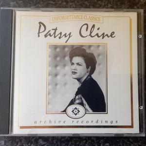 May include: A CD case featuring Patsy Cline's album, "Unforgettable Classics." The cover has a black and white photo of Patsy Cline. The text includes "Unforgettable Classics," "Patsy Cline," and "archive recordings."