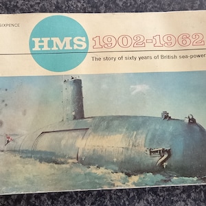 May include: A vintage book cover with a blue circle that says "HMS" and the text "1902-1962" in red. The book cover also says "The story of sixty years of British sea-power". The cover features a blue submarine in the water.
