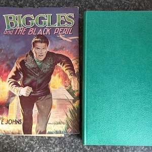 May include: A vintage book titled "Biggles and the Black Peril" with a colorful cover illustration of a man running from a fire. Next to it is a solid green hardcover book.
