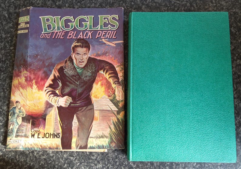 May include: A vintage book titled "Biggles and the Black Peril" with a colorful cover illustration of a man running from a fire. Next to it is a solid green hardcover book.
