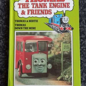 Puede incluir: Una cubierta de libro verde con el título "Thomas the Tank Engine & Friends" en letras rojas y blancas. El libro presenta ilustraciones de Thomas the Tank Engine y un autobús rojo con una cara.