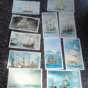 May include: A collection of rectangular cards featuring watercolor paintings of sailing ships. The ships are depicted with billowing white sails against a backdrop of blue skies and seas. The cards vary in size and ship design.