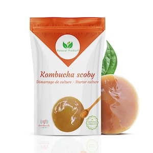 Pode incluir: Uma bolsa branca com a parte superior vermelha, etiquetada como "Kombucha scoby" e "Natural Probio", contém uma cultura inicial para fazer kombucha. A bolsa está ao lado de um scoby redondo, de cor marrom claro e translúcido.