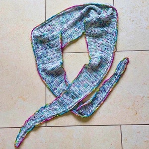 Peut inclure: Une écharpe en crochet blanche avec une bordure multicolore. L'écharpe est réalisée avec un point simple et a une forme longue et fluide.