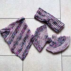 Könnte beinhalten: Ein Set handgestrickter Accessoires in Rosa-, Lila- und Blautönen. Das Set umfasst einen Schal, ein Stirnband und ein Paar Fäustlinge. Die Artikel sind mit einem strukturierten Stich gefertigt und auf einer hell gefliesten Oberfläche angeordnet.