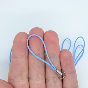 May include: A light blue phone strap with a silver metal ring and a silver metal clasp.