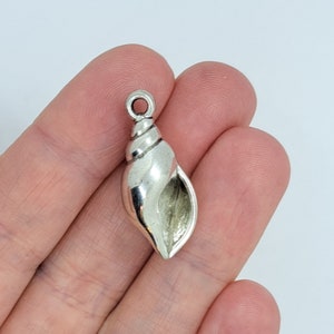May include: A silver seashell charm with a loop for attaching to jewellery. The shell has a spiral design and a polished finish. The charm is approximately 3.8 cm long.