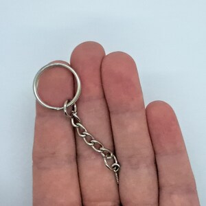 May include: A silver key chain with a round ring and a chain link. The chain is held in a hand.