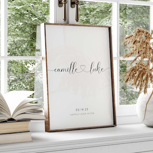 May include: A framed print with a white background and black text. The text reads "camille & luke" with a heart symbol between the names. Below the names is the date "02.14.22" and the text "happily ever after".
