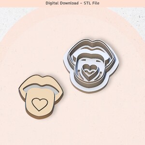 May include: Two cookie cutters in the shape of a mouth with a tongue sticking out. The tongue has a heart on it. The cookie cutters are made of metal and are silver in color.