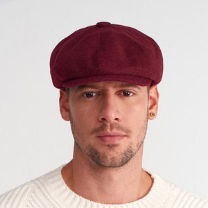May include: A burgundy wool newsboy cap with a rounded crown and a flat brim.