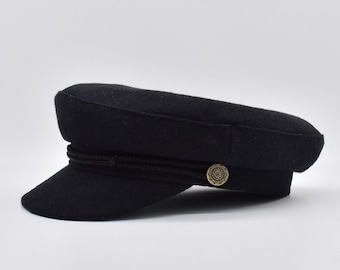 Könnte beinhalten: Eine schwarze Wollmütze im Matrosen-Stil mit einem braunen geflochtenen Band und einem goldenen Knopf.