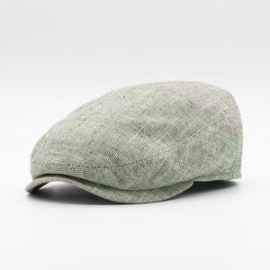 May include: A light green newsboy cap made of a textured fabric. The cap has a curved brim and a rounded crown. The fabric appears to be a linen blend. The cap is a neutral color and could be worn by anyone.