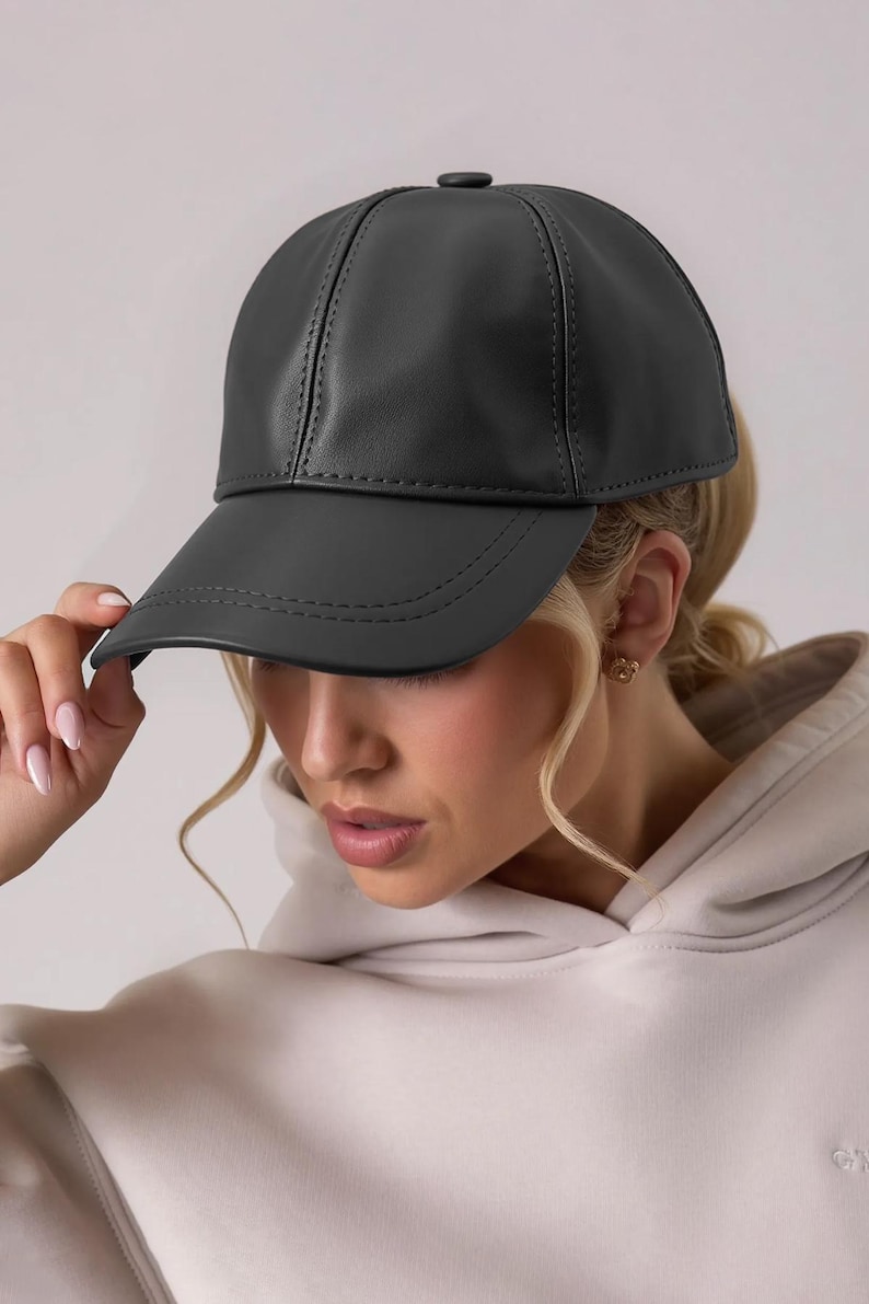 May include: A black baseball cap made of a smooth material. The cap has a curved brim and a structured crown with visible stitching details. The cap is a solid color and appears to be made of leather or a leather-like material.