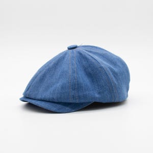 Puede incluir: Una gorra de golf de denim azul con un botón en la parte superior.