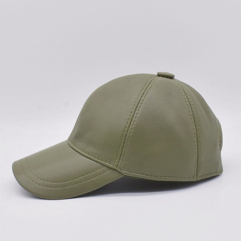May include: Olive green baseball cap with a curved brim. The cap is made of a smooth material and features a button on top. The cap has a classic six-panel design with stitched seams.