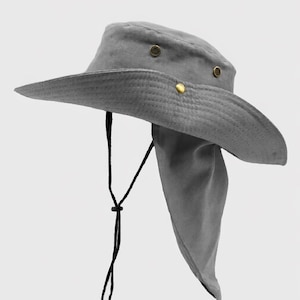 Könnte beinhalten: Grauer Sonnenhut mit breiter Krempe und Nackenschutz. Der Hut hat einen schwarzen Kinnriemen und messingfarbene Nieten. Dieser Hut ist für Sonnenschutz und Outdoor-Aktivitäten konzipiert.