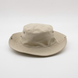 May include: A beige sun hat with a wide brim and a rounded crown. The hat features a series of small metal eyelets around the crown and a structured brim. The hat is designed to provide shade and protection from the sun.