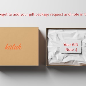 May include: A brown cardboard box with the word "k&uuml;lah" printed on it. The box is open and a white tissue paper-filled box is inside. The tissue paper is crumpled and a white card with the text "Your Gift Note :)" is on top of the tissue paper.