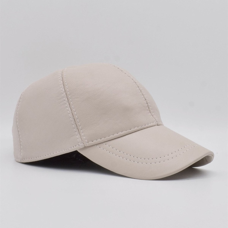 May include: A light beige baseball cap made of leather. The cap has a curved brim and is stitched with white thread. The design is simple and classic, suitable for casual wear. The cap is a neutral color.