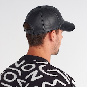 May include: A black leather baseball cap with a curved brim. The cap is worn backwards on a person's head.