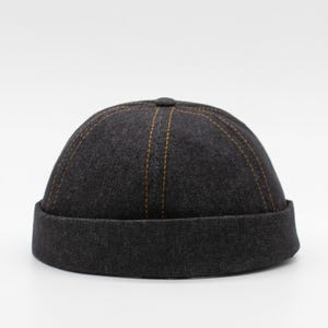 May include: A black denim newsboy cap with brown stitching detail.