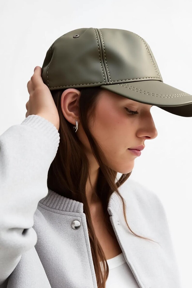 May include: Olive green baseball cap with a curved brim and stitched detailing. The cap is made of a smooth material and has a classic design. The cap is a stylish accessory for casual wear.