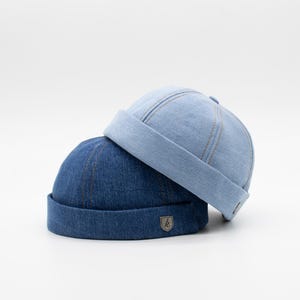 May include: Two denim bucket hats, one light blue and one dark blue. The darker blue hat has a small metal logo with the letter "k" on the front.