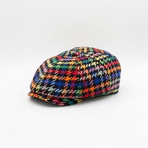 May include: A colorful, multi-colored, patterned newsboy cap with a black background. The pattern is a houndstooth design with red, yellow, blue, green, and pink accents.
