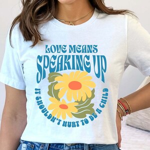 Könnte beinhalten: Weißes T-Shirt mit einem blauen und gelben Gänseblümchen-Motiv und dem Text "Love Means Speaking Up It Shouldn't Hurt To Be A Child."