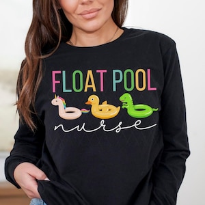 May include: Black long-sleeve shirt with the text "FLOAT POOL nurse" in rainbow colors. The text is surrounded by images of inflatable pool toys, including a unicorn, a duck, and a dinosaur.