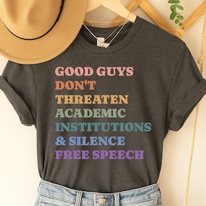 May include: A dark grey t-shirt with the text "GOOD GUYS DON'T THREATEN ACADEMIC INSTITUTIONS & SILENCE FREE SPEECH" printed in rainbow colours.