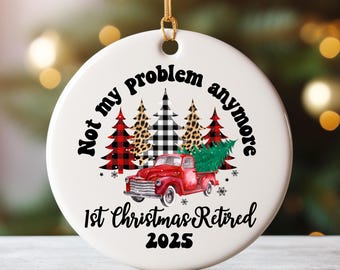 May include: Round white Christmas tree decoration with a red truck carrying a fir tree. The ornament features the text "Not my problem anymore" and "1st Christmas Retired 2025". The design includes trees with plaid and leopard print patterns.
