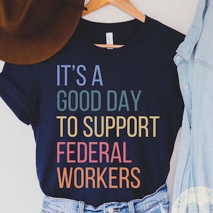 May include: A navy blue t-shirt with the text "It's a good day to support federal workers" in rainbow colours.