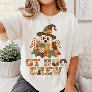 Puede incluir: Una camiseta de manga corta color marfil con el gráfico de un fantasma con sombrero de bruja, diseñado con un patrón de patchwork en tonos naranja, marrón y verde. Debajo del fantasma, el texto OT BOO CREW aparece en un estilo patchwork.