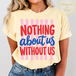 May include: A pale yellow short-sleeve t-shirt featuring a graphic design with vertical pink stripes. The text reads NOTHING in red, about us in blue, and WITHOUT US in red. The shirt is paired with blue denim jeans with a visible metal button.