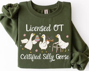 Może przedstawiać: Zielona bluza w kolorze wojskowym z napisem "Licensed OT Certified Silly Goose" i grafiką trzech gęsi z kreskówek. Gęsi trzymają zabawki i chodzik. Obecne są różowe kwiaty.