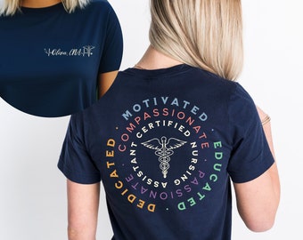 May include: Navy blue t-shirt with a circular design on the back featuring the words "Motivated, Compassionate, Certified, Educated, Dedicated, Constant, Nursing, Passionate, Assisted." A medical symbol is in the center. The front of the shirt has the text "Oliva, MA" and a medical symbol.