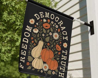 May include: A black rectangular garden flag featuring the text FREEDOM DEMOCRACY TRUTH in a curved cream font. The centre displays a botanical illustration of three pumpkins in orange and cream, surrounded by various flowers and green leaves.