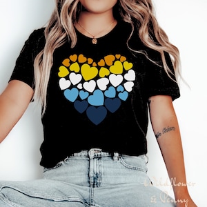 May include: A black t-shirt with a large heart design made up of smaller hearts in shades of yellow, white, blue, and navy.