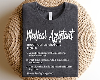 May include: A dark gray t-shirt with white text that reads "Medical Assistant" and a definition of the term. The definition includes the phrase "They're kind of a big deal."
