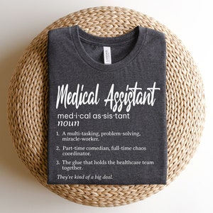 May include: A dark gray t-shirt with white text that reads "Medical Assistant" and a definition of the term. The definition includes the phrase "They're kind of a big deal."
