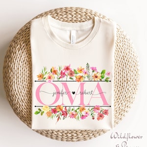 Puede incluir: Una camiseta blanca con un diseño floral rosa y la palabra "OMA" en rosa con los nombres "jennifer" y "robert" escritos en cursiva negra.