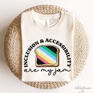 May include: A white t-shirt with the text "Inclusion & Accessibility are my jam" in black. The text is in a circle around a cartoon image of a slice of bread with rainbow colored jam.