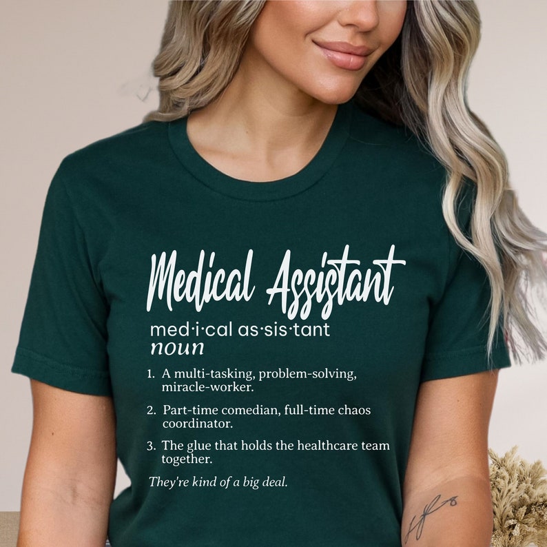 May include: A dark green t-shirt with white text that reads "Medical Assistant" and a definition of the word. The definition includes the phrase "They're kind of a big deal."